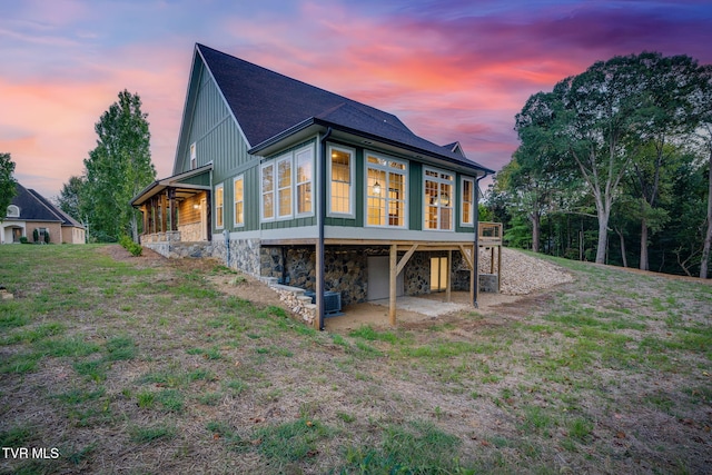 back of house with stone siding, a lawn, board and batten siding, and a wooden deck