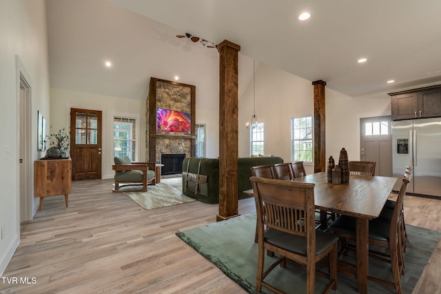 dining room with ornate columns, light wood-style flooring, high vaulted ceiling, and a stone fireplace