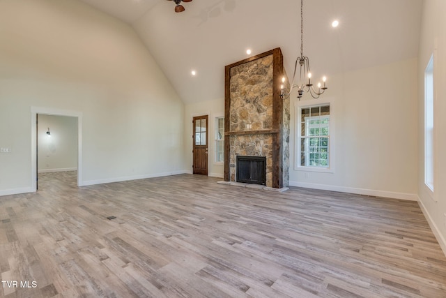 unfurnished living room with baseboards, an inviting chandelier, light wood-style floors, a fireplace, and high vaulted ceiling