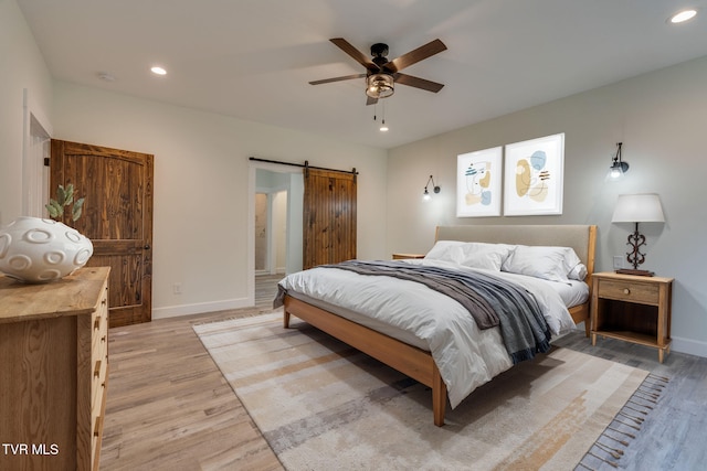 bedroom with light wood-style floors, recessed lighting, baseboards, and a barn door