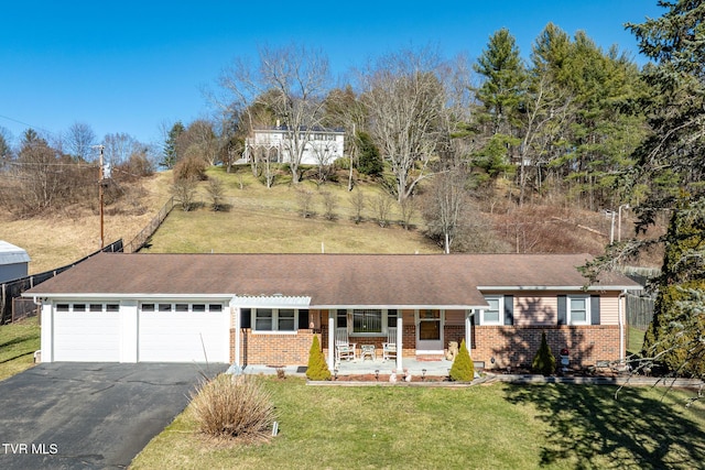 single story home with a porch, aphalt driveway, an attached garage, brick siding, and a front yard