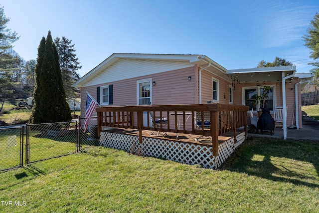 rear view of house with a deck, a yard, fence, and a gate