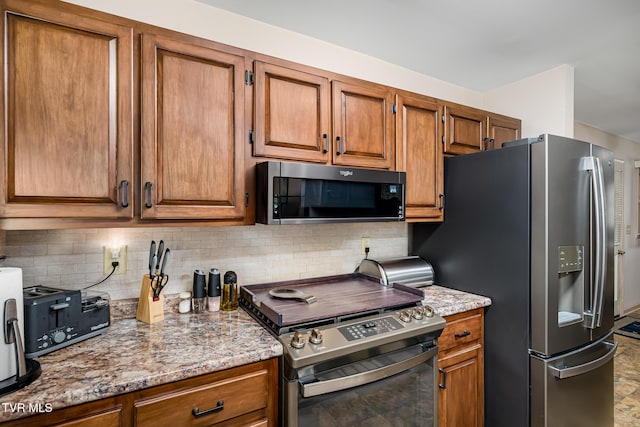 kitchen with appliances with stainless steel finishes, brown cabinetry, light stone counters, and decorative backsplash