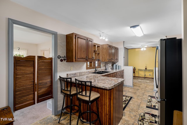 kitchen featuring a breakfast bar, freestanding refrigerator, a peninsula, open shelves, and a sink