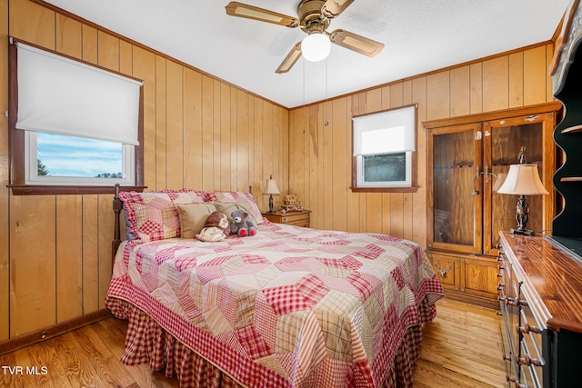 bedroom with a textured ceiling, wood walls, a ceiling fan, light wood-style floors, and ornamental molding