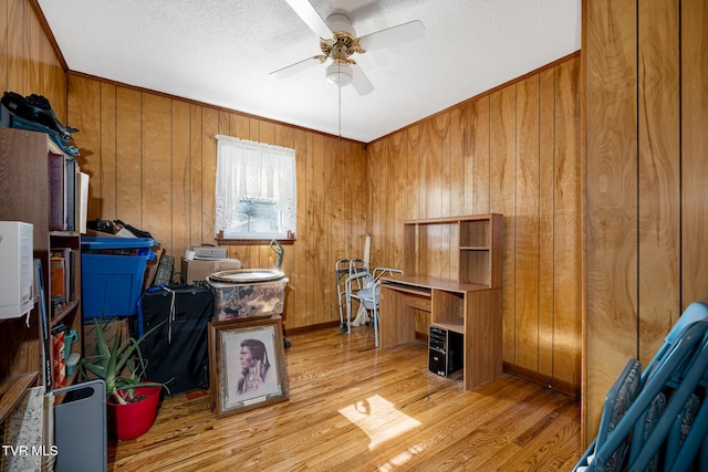 office featuring light wood finished floors, wooden walls, baseboards, a ceiling fan, and a textured ceiling