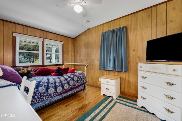 bedroom featuring wooden walls, vaulted ceiling, light wood-style flooring, and a ceiling fan