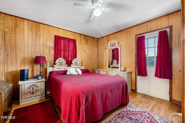 bedroom with visible vents, a ceiling fan, wood walls, a textured ceiling, and wood finished floors