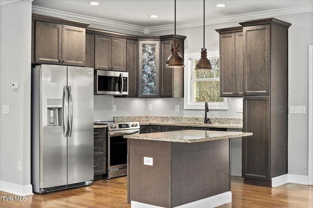 kitchen with pendant lighting, ornamental molding, a center island, stainless steel appliances, and light stone countertops