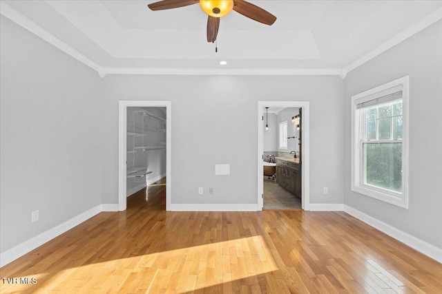 unfurnished bedroom with light hardwood / wood-style flooring, a walk in closet, a tray ceiling, ensuite bath, and a closet