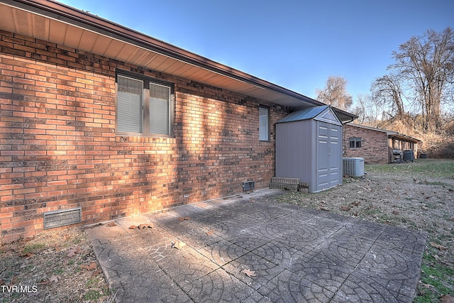 view of side of home with central AC unit, a shed, and a patio area