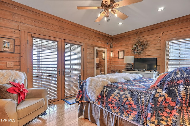 bedroom with wood walls, access to exterior, ceiling fan, light hardwood / wood-style floors, and french doors