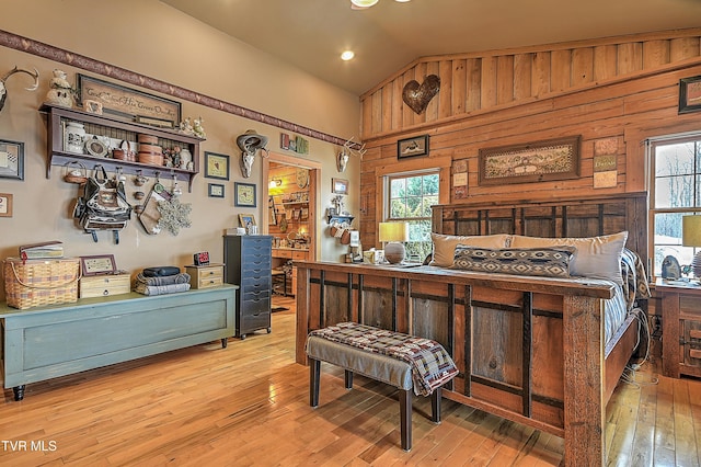 bedroom featuring vaulted ceiling, wooden walls, and light hardwood / wood-style flooring