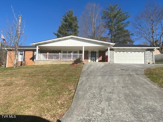 single story home featuring a garage, covered porch, and a front yard