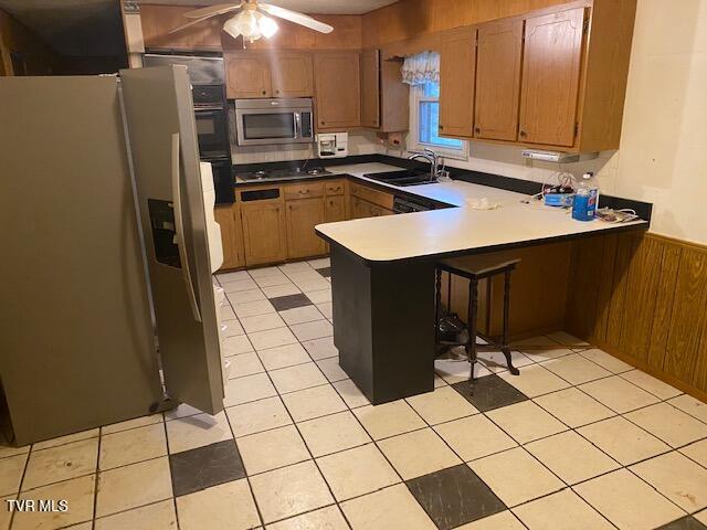 kitchen with wood walls, sink, ceiling fan, kitchen peninsula, and stainless steel appliances