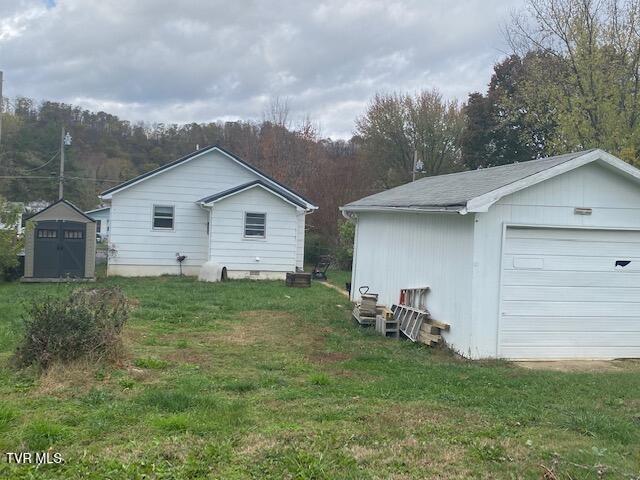 view of property exterior featuring an outbuilding, a lawn, a garage, and a view of trees