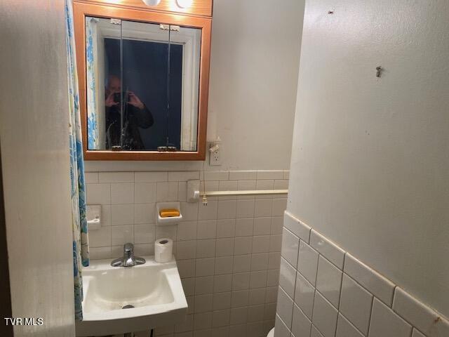 bathroom with a wainscoted wall, a sink, and tile walls