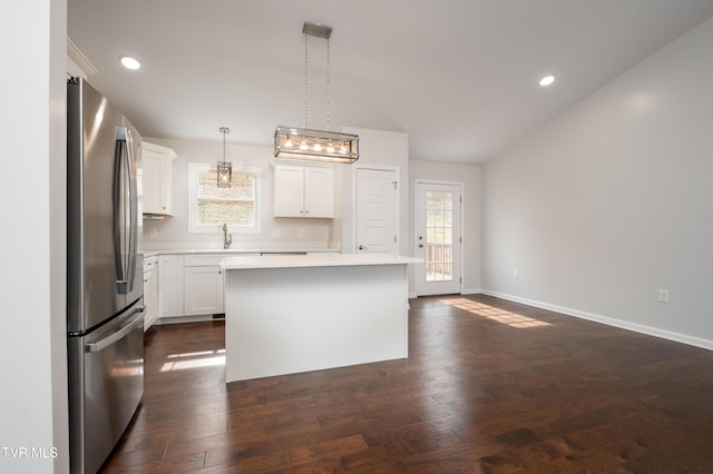 kitchen with dark wood-type flooring, decorative light fixtures, stainless steel refrigerator, a kitchen island, and white cabinets