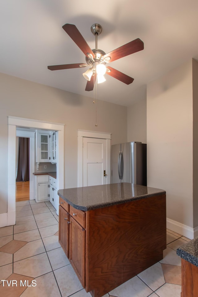 kitchen with light tile patterned flooring, dark stone countertops, stainless steel fridge, and ceiling fan