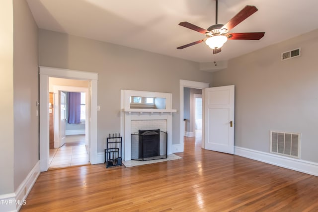 unfurnished living room featuring ceiling fan, a fireplace, and light wood-type flooring