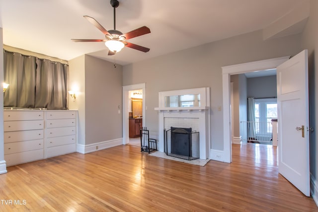 unfurnished living room with ceiling fan, a brick fireplace, and light wood-type flooring