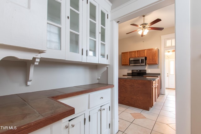 kitchen featuring range with electric stovetop, light tile patterned floors, white cabinets, ceiling fan, and a high ceiling