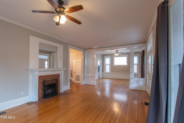 unfurnished living room featuring ceiling fan, ornamental molding, a tiled fireplace, and light hardwood / wood-style floors