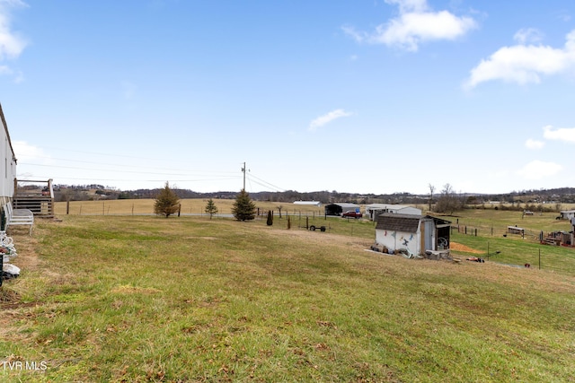 view of yard with fence, an outbuilding, and a rural view