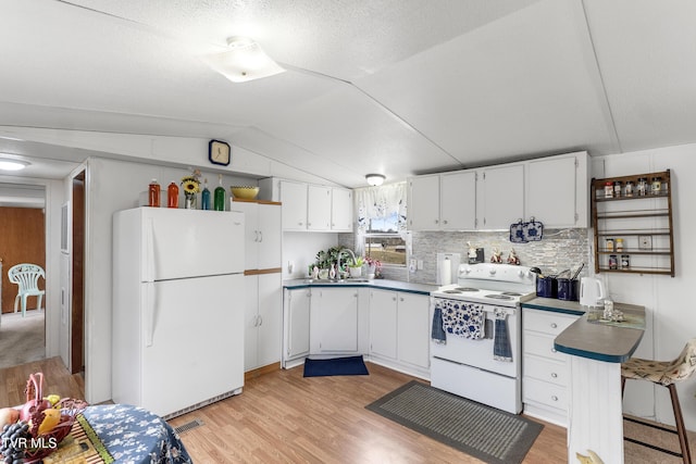 kitchen with white appliances, a sink, white cabinetry, light wood-style floors, and vaulted ceiling