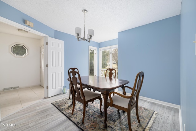 dining area featuring a textured ceiling, light hardwood / wood-style floors, and a chandelier