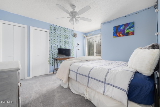 carpeted bedroom featuring ceiling fan, two closets, and a textured ceiling