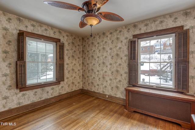 empty room featuring ceiling fan, radiator heating unit, light hardwood / wood-style floors, and a healthy amount of sunlight