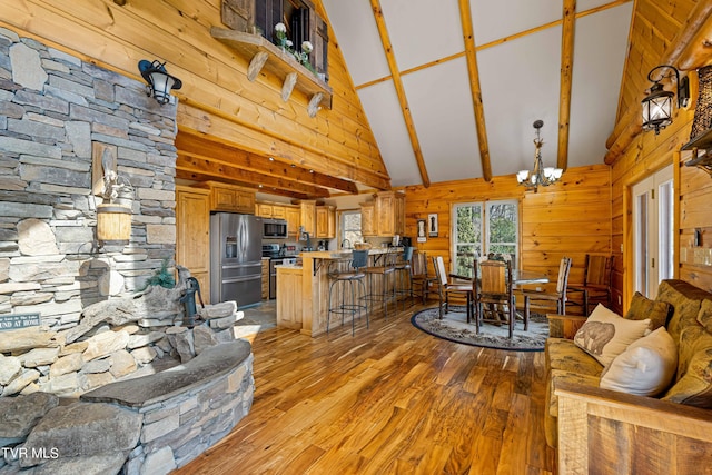 living room with an inviting chandelier, high vaulted ceiling, wooden walls, beamed ceiling, and light hardwood / wood-style floors