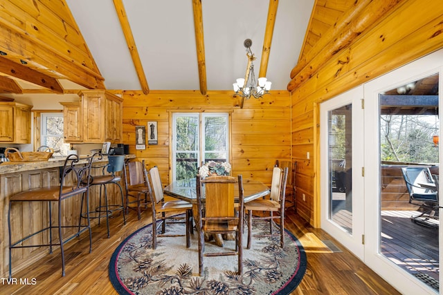 dining space with a wealth of natural light, wood walls, lofted ceiling with beams, dark hardwood / wood-style flooring, and a notable chandelier