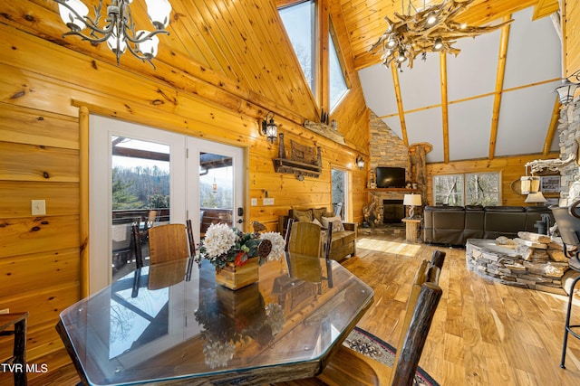 dining area with a notable chandelier, a stone fireplace, plenty of natural light, and wood walls