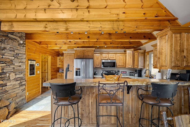 kitchen featuring a breakfast bar, wooden walls, stainless steel appliances, kitchen peninsula, and beamed ceiling