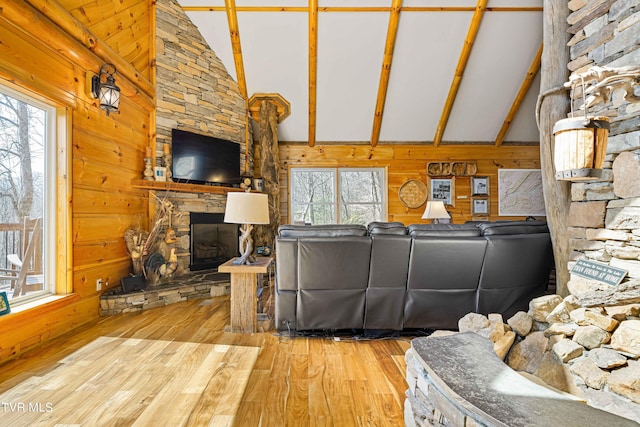 living room with wooden walls, plenty of natural light, a stone fireplace, and light hardwood / wood-style floors