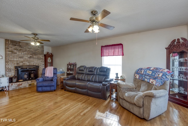 living room with ceiling fan, a wood stove, a textured ceiling, and light wood-type flooring