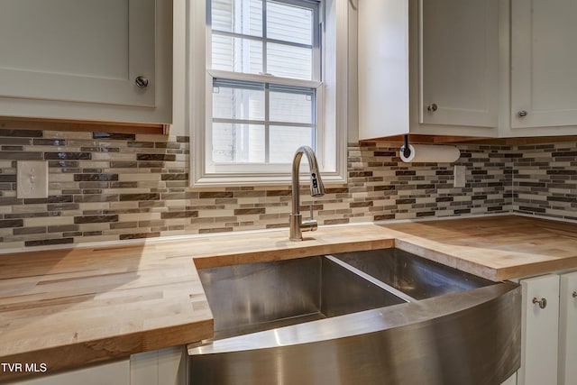 kitchen with white cabinetry, wood counters, sink, and backsplash