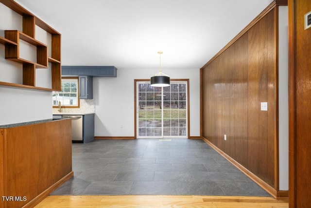 kitchen featuring tasteful backsplash, wooden walls, dishwasher, and pendant lighting