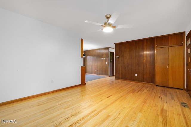 interior space with wooden walls, light hardwood / wood-style floors, and ceiling fan