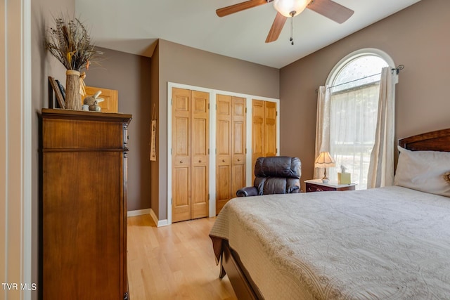 bedroom with ceiling fan, light hardwood / wood-style flooring, and multiple closets