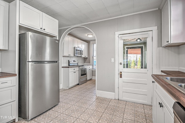 kitchen with crown molding, stainless steel appliances, butcher block countertops, and white cabinets