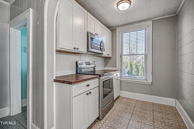 kitchen with butcher block counters, wood walls, white cabinets, and appliances with stainless steel finishes