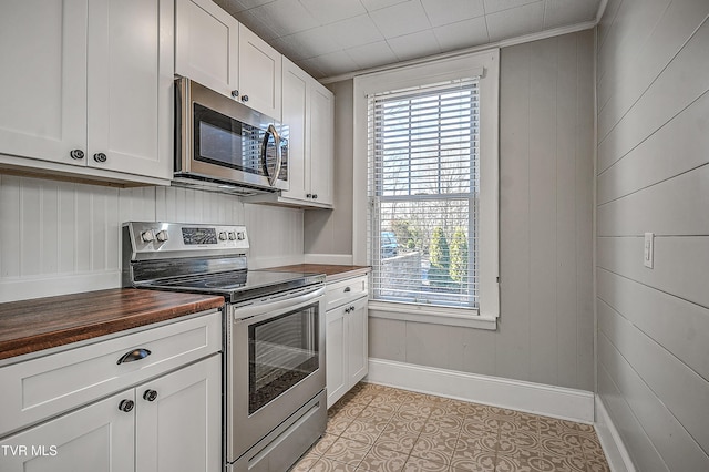 kitchen with butcher block counters, wood walls, light tile patterned floors, stainless steel appliances, and white cabinets