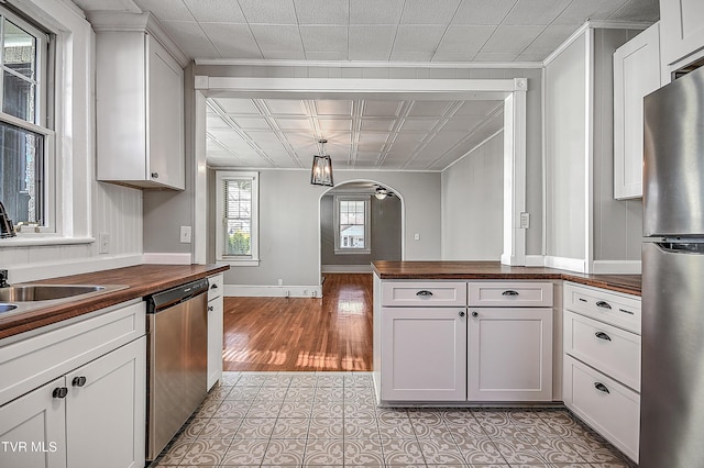 kitchen with wooden counters, stainless steel appliances, light hardwood / wood-style floors, white cabinets, and decorative light fixtures