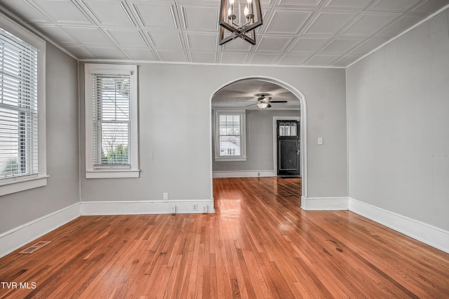 unfurnished room featuring ceiling fan with notable chandelier, wood-type flooring, a baseboard radiator, and a wealth of natural light