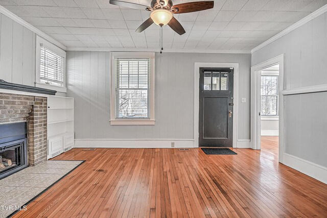 entrance foyer featuring crown molding, ceiling fan, a fireplace, and light wood-type flooring