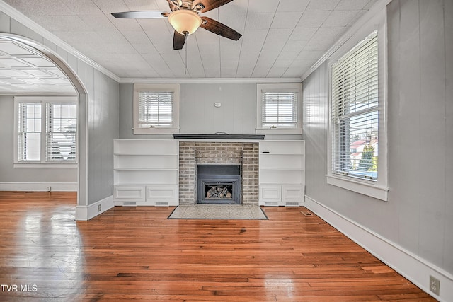 unfurnished living room featuring hardwood / wood-style floors, ceiling fan, crown molding, a brick fireplace, and built in shelves