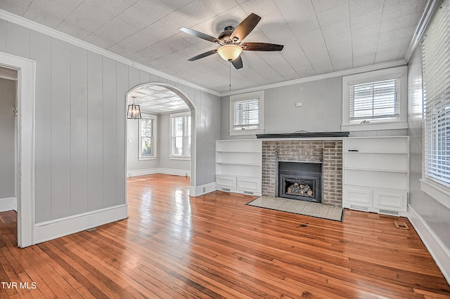 unfurnished living room with a brick fireplace, ornamental molding, built in features, hardwood / wood-style flooring, and ceiling fan